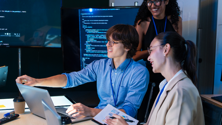 Three people looking at a computer with a data screen in the background